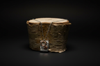 A handmade pendant necklace with a hammered silver rectangular plate, a copper ring, and a copper sphere, draped over a birch log on a black background.