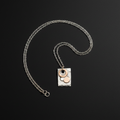 A silver chain necklace with a rectangular silver pendant featuring a hammered finish, adorned with three circular elements in silver, rose gold, and white, displayed on a dark background.