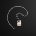 A silver chain necklace with a rectangular silver pendant featuring a hammered finish, adorned with three circular elements in silver, rose gold, and white, displayed on a dark background.