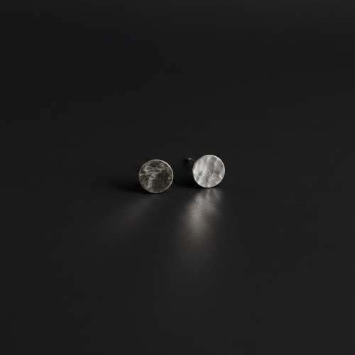 A pair of small round stud earrings with a hammered silver finish, displayed on a dark, reflective surface.