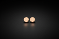 A pair of small round rose gold stud earrings with a textured, hammered finish, displayed on a dark reflective surface.