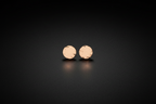 A pair of small round rose gold stud earrings with a textured, hammered finish, displayed on a dark reflective surface.