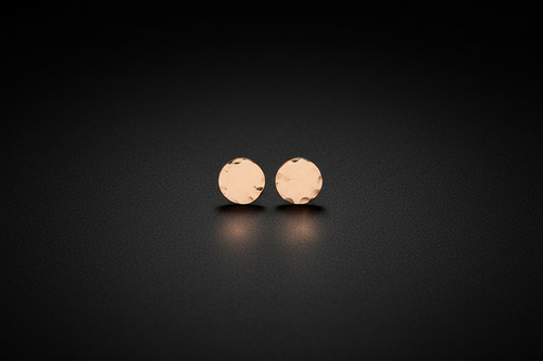 A pair of small round rose gold stud earrings with a textured, hammered finish, displayed on a dark reflective surface.