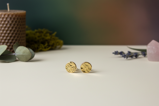 Golden Charm Studs by Jewellery by JN, hammered brass circles with sterling silver posts, shown front-facing on a creamy background.