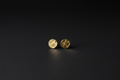 A pair of small round gold stud earrings with a textured hammered finish, displayed on a dark black background.