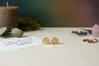 Golden Charm Studs by Jewellery by JN in branded packaging with a handwritten affirmation card and ritual props on an earthy background.