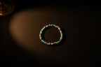 A beaded bracelet with turquoise-blue and cream-colored round beads, arranged in a circle on a dark brown surface under dramatic warm lighting.