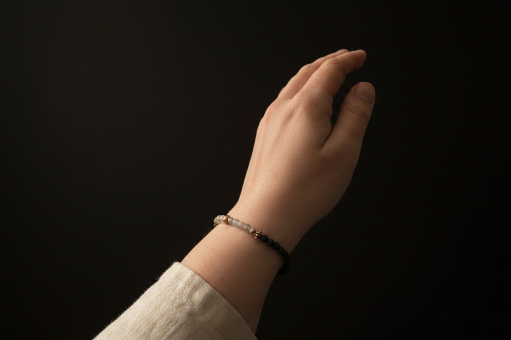 A close-up of a person's hand and wrist wearing a beaded bracelet with black and silver beads, set against a solid black background.