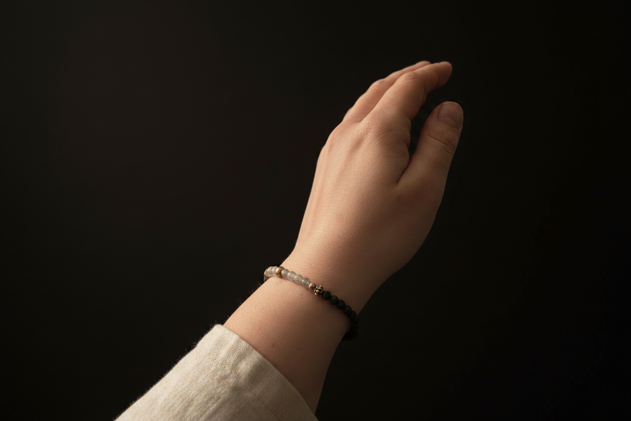 A close-up of a person's hand and wrist wearing a beaded bracelet with black and silver beads, set against a solid black background.