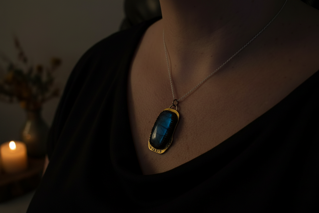 A close-up lifestyle shot of a person wearing a gold pendant necklace with a dark blue iridescent stone, set against a dark background with a blurred candle on the left.