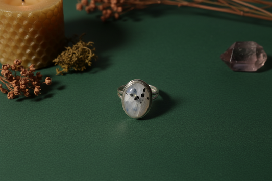 Silver ring with a stone on a green surface with candles and dried plants.