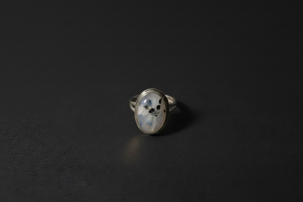 A silver ring with an oval-shaped cabochon gemstone featuring a black cat print, displayed on a dark textured surface.
