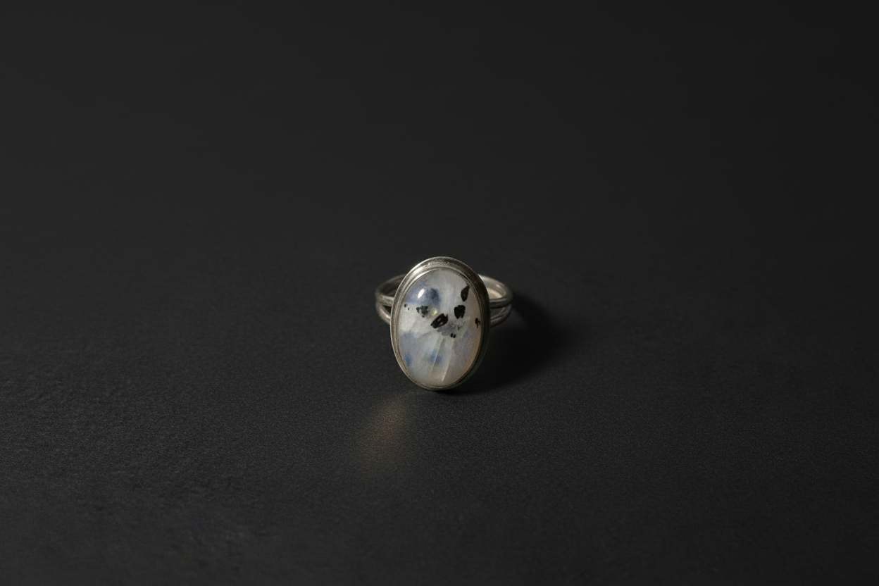 A silver ring with an oval-shaped cabochon gemstone featuring a black cat print, displayed on a dark textured surface.