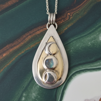 Teardrop-shaped pendant with gold and silver design on a green marbled background
