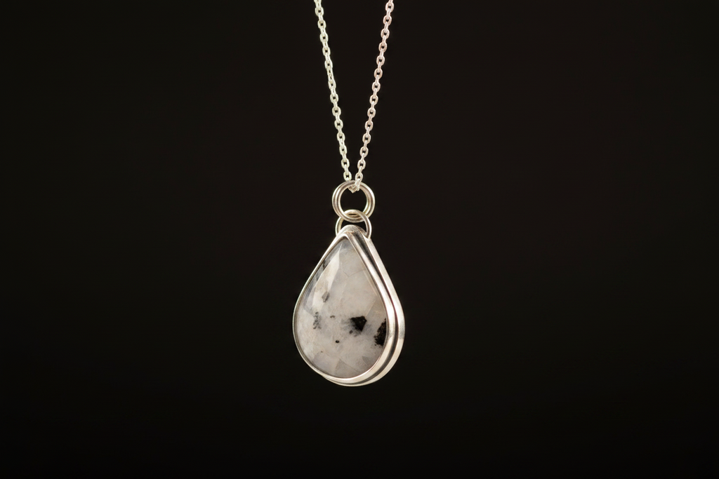 A silver teardrop pendant necklace featuring a white gemstone with black inclusions, suspended from a delicate silver chain against a solid black background.