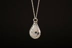 A silver teardrop pendant necklace featuring a white gemstone with black inclusions, suspended from a delicate silver chain against a solid black background.