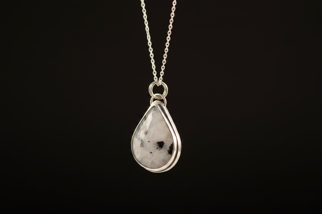 A silver teardrop pendant necklace featuring a white gemstone with black inclusions, suspended from a delicate silver chain against a solid black background.