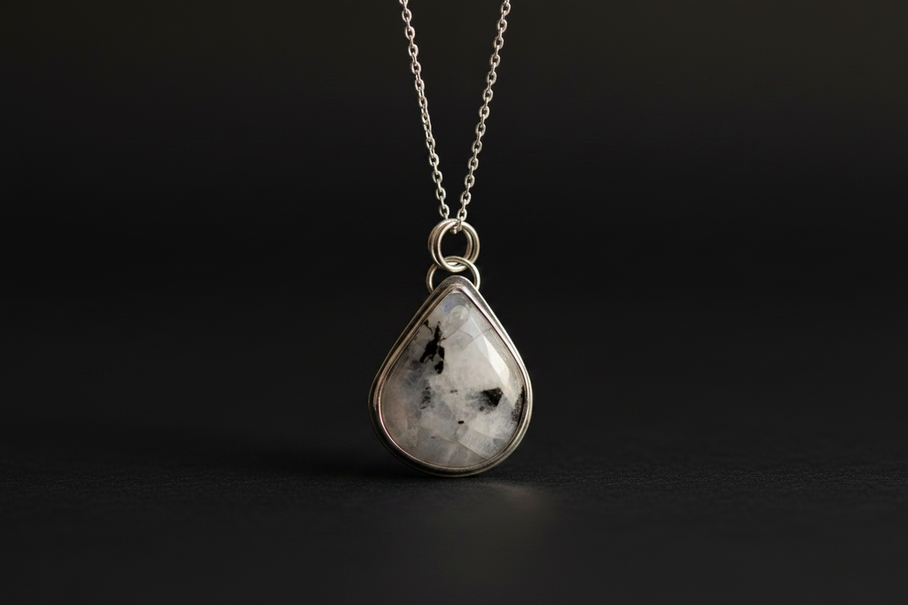 A silver teardrop pendant necklace featuring a polished black-and-white marbled stone, suspended from a delicate silver chain against a dark background.