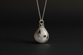 A silver teardrop pendant necklace featuring a polished black-and-white marbled stone, suspended from a delicate silver chain against a dark background.