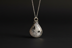 A silver teardrop pendant necklace featuring a polished black-and-white marbled stone, suspended from a delicate silver chain against a dark background.