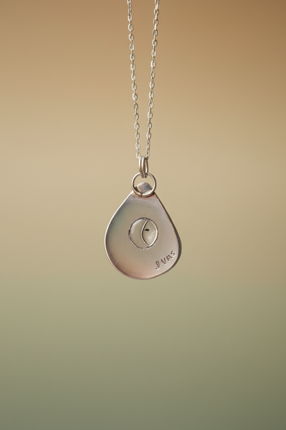Silver necklace with a teardrop-shaped pendant on a beige background