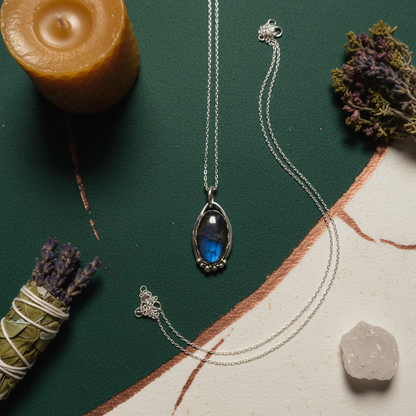 Necklace with a blue pendant on a green surface with a candle and herbs.