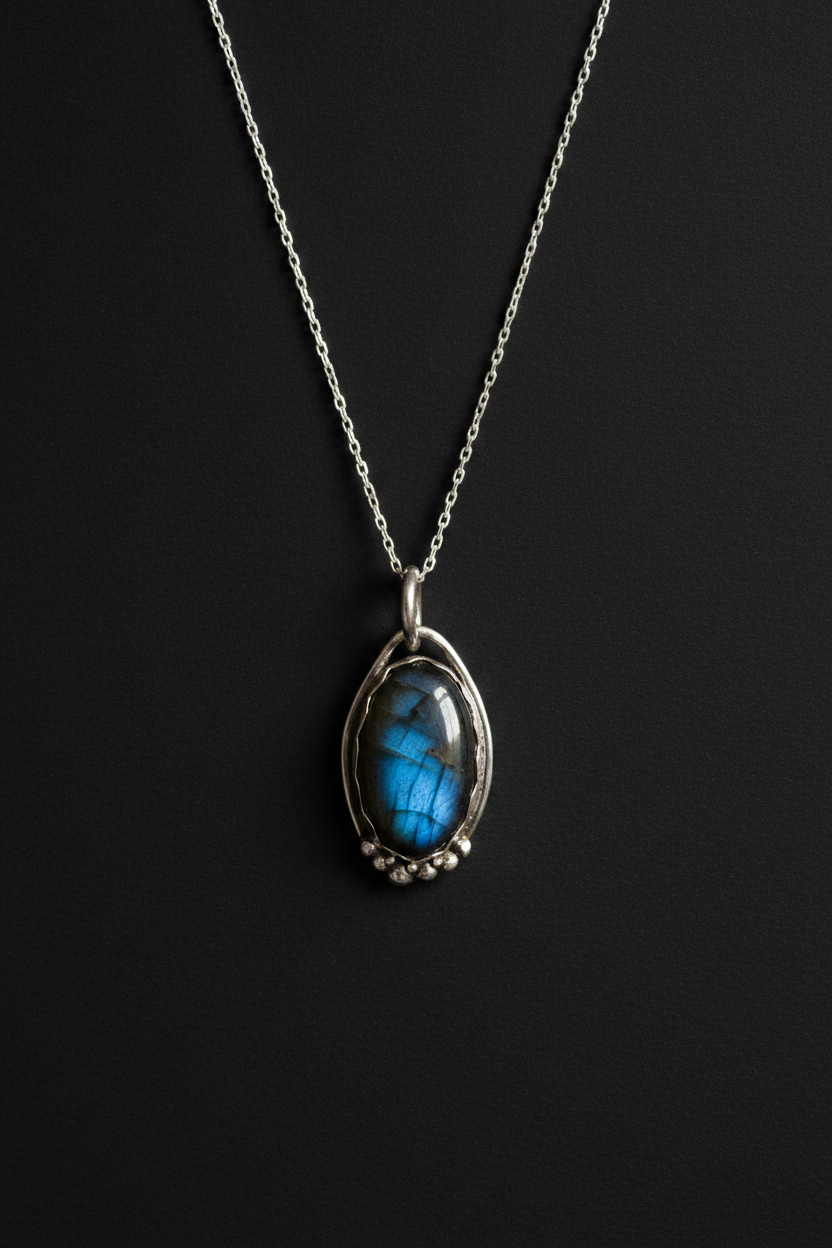 A silver chain necklace with a teardrop-shaped pendant featuring a vibrant blue labradorite stone in a silver bezel setting, displayed against a dark black background.