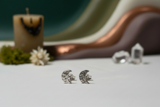 Silver moon-shaped earrings on a white surface with decorative items in the background.
