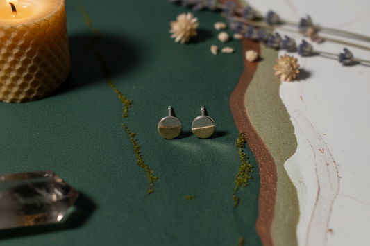 Gold earrings on a textured surface with a candle and decorative elements.