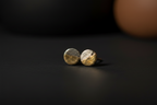A pair of small round stud earrings with a split gold and silver finish, resting on a dark surface.