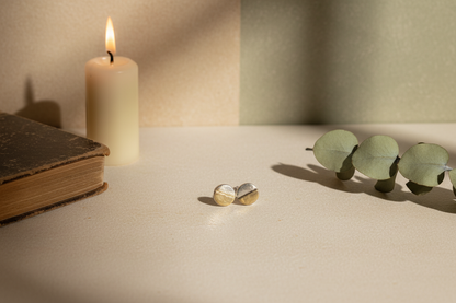 Gold earrings on a surface with a candle and green leaves in the background