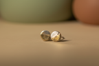 Gold stud earrings on a beige surface with a blurred background