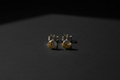 A pair of small gold and silver crescent moon stud earrings resting on a dark, textured surface under dramatic, low-angle lighting.