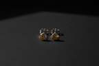 A pair of small gold and silver crescent moon stud earrings resting on a dark, textured surface under dramatic, low-angle lighting.