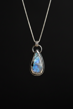 A teardrop-shaped labradorite pendant necklace in a silver bezel setting on a delicate silver chain, displayed against a solid black background.
