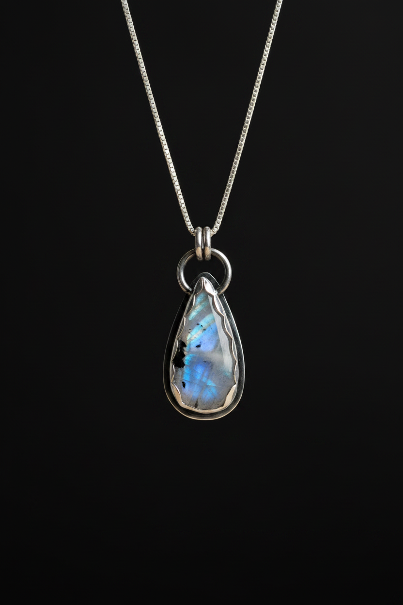 A teardrop-shaped labradorite pendant necklace in a silver bezel setting on a delicate silver chain, displayed against a solid black background.