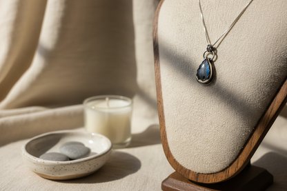 Necklace with a pendant on a wooden stand next to a candle and stones on a textured surface.