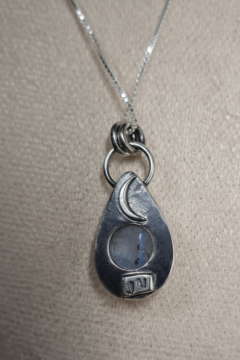 Silver pendant with moon and sun design on a beige background