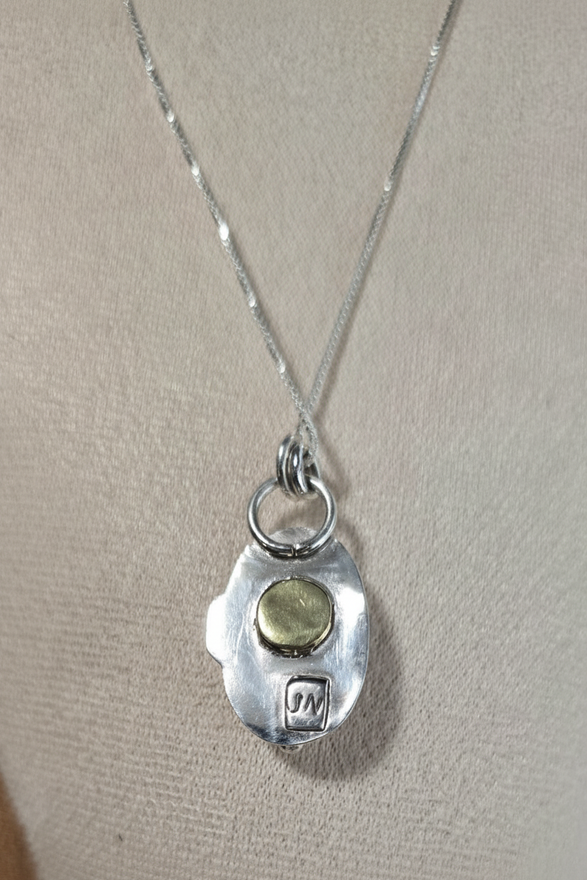 Silver necklace with a pendant featuring a green stone on a beige background
