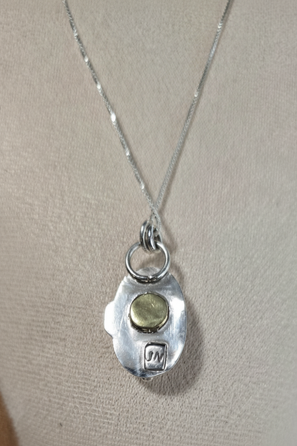 Silver necklace with a pendant featuring a green stone on a beige background
