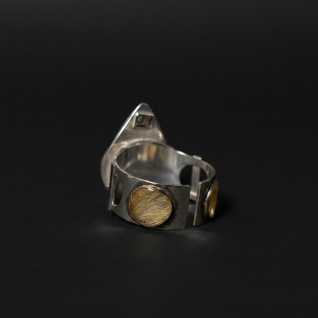 A silver-toned geometric ring with circular gold-toned inlays, photographed on a dark black background.
