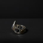 A silver-toned metal ring with a unique slotted band design and a small round gold-toned accent, photographed on a dark black background.
