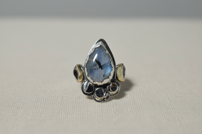 Silver ring with a teardrop-shaped blue gemstone on a light gray background