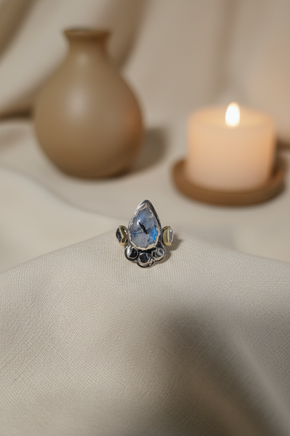 Silver ring with a blue gemstone on a beige fabric background with a candle and vase.