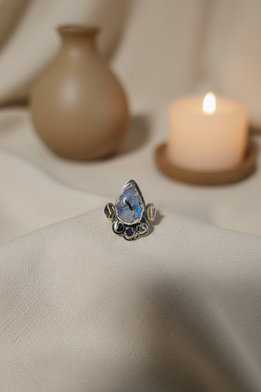 Silver ring with a blue gemstone on a beige fabric background with a candle and vase.
