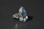 A sterling silver ring featuring a teardrop-shaped blue labradorite gemstone, accented with small round white stones and a crescent moon detail on the band, set against a dark gray background.