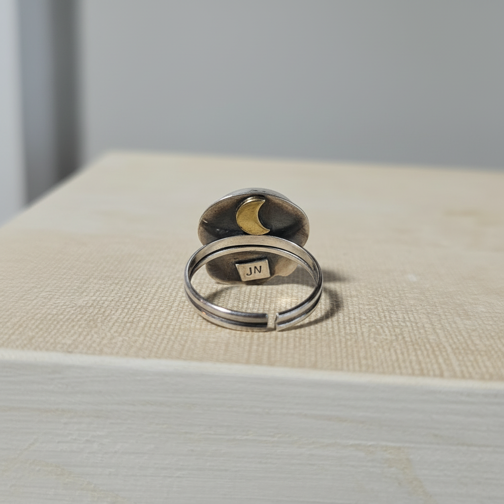 Silver ring with moon design on a textured surface