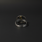Two silver-toned open stretch rings stacked together on a dark black background. The top ring features a small gold crescent moon inlay, and the bottom ring has a small square brand plaque inside.