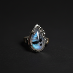 A sterling silver ring featuring a teardrop-shaped labradorite gemstone that displays a blue and white iridescent flash, set against a dark background.