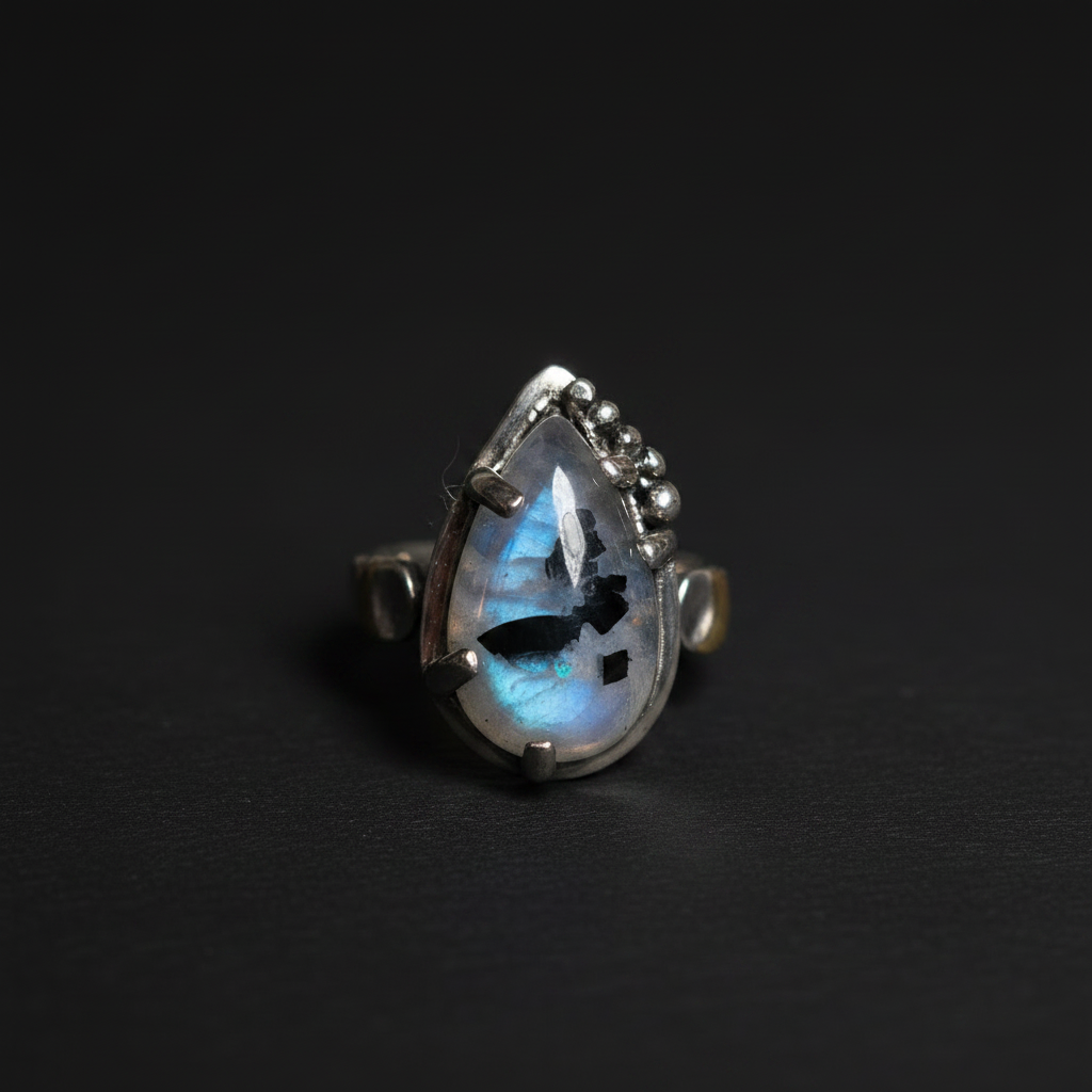 A sterling silver ring featuring a teardrop-shaped labradorite gemstone that displays a blue and white iridescent flash, set against a dark background.